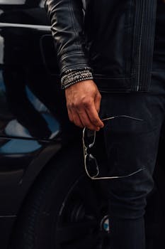 一名男子身穿皮夹克，戴着手镯和太阳镜，坐在车旁