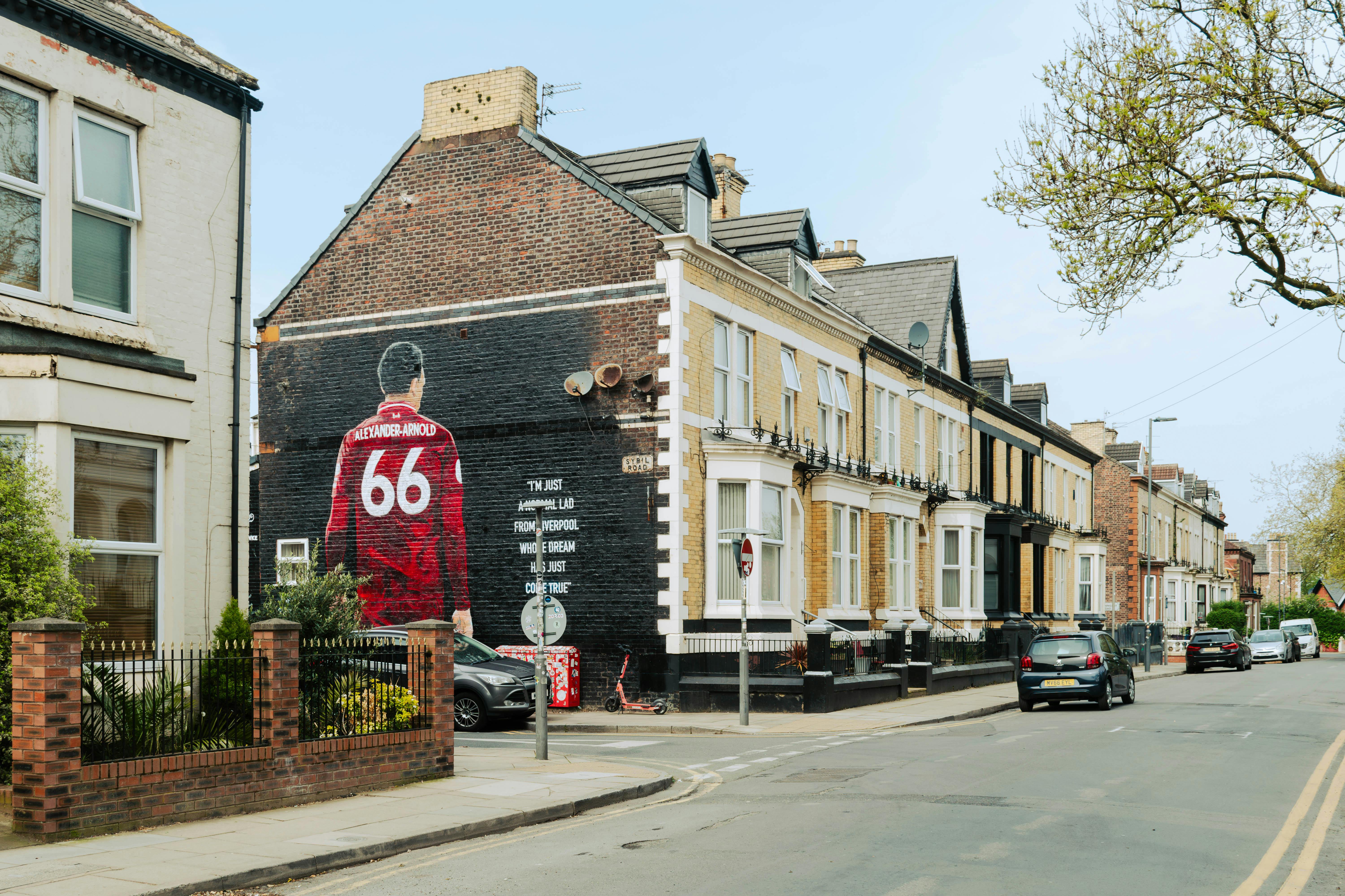 Urban street scene in Liverpool featuring a prominent mural of Trent Alexander-Arnold.