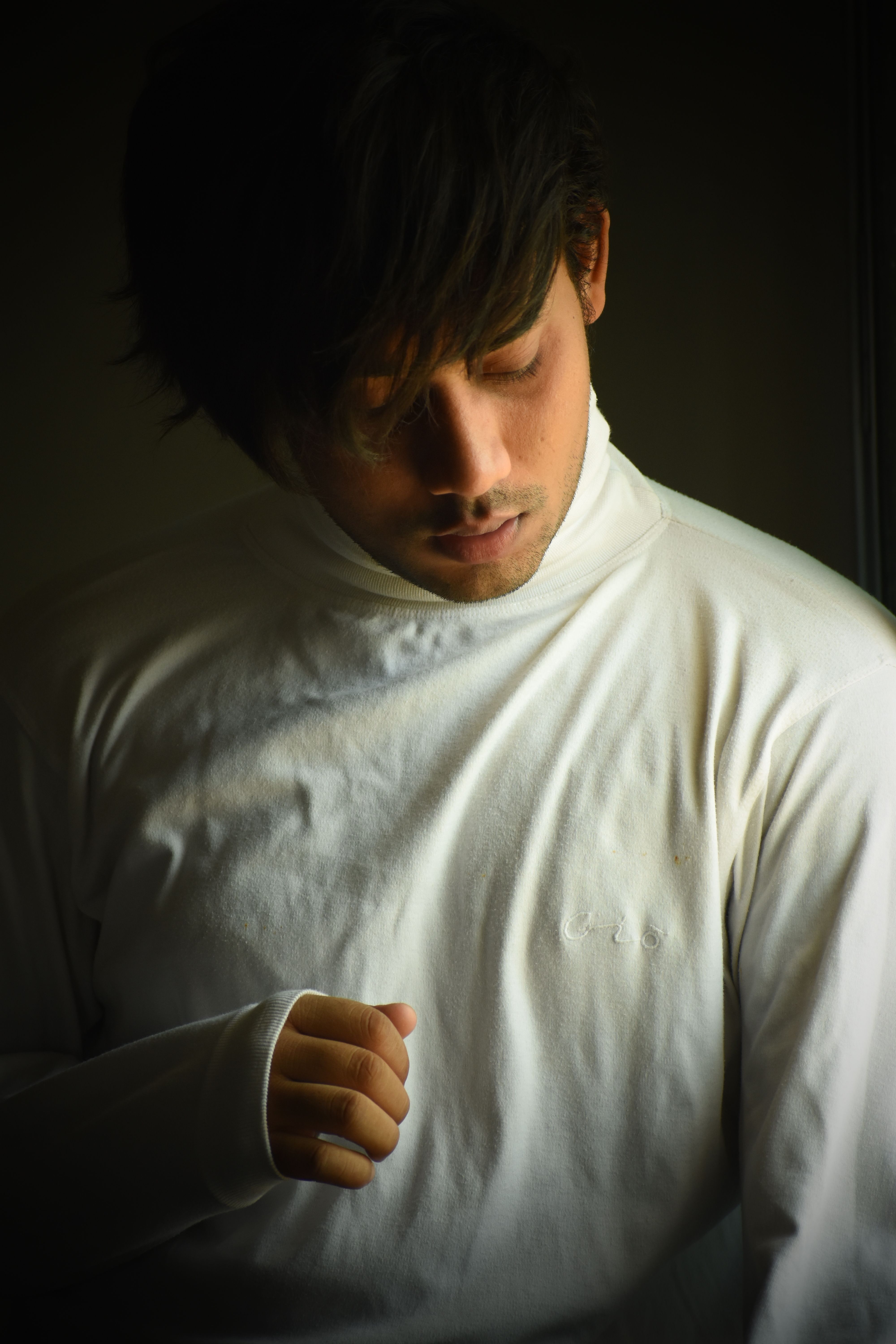 A contemplative young man in a white turtleneck poses against a dark background.