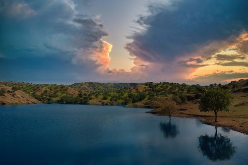 Free Picturesque sunset with dramatic clouds over a peaceful countryside lake. Stock Photo