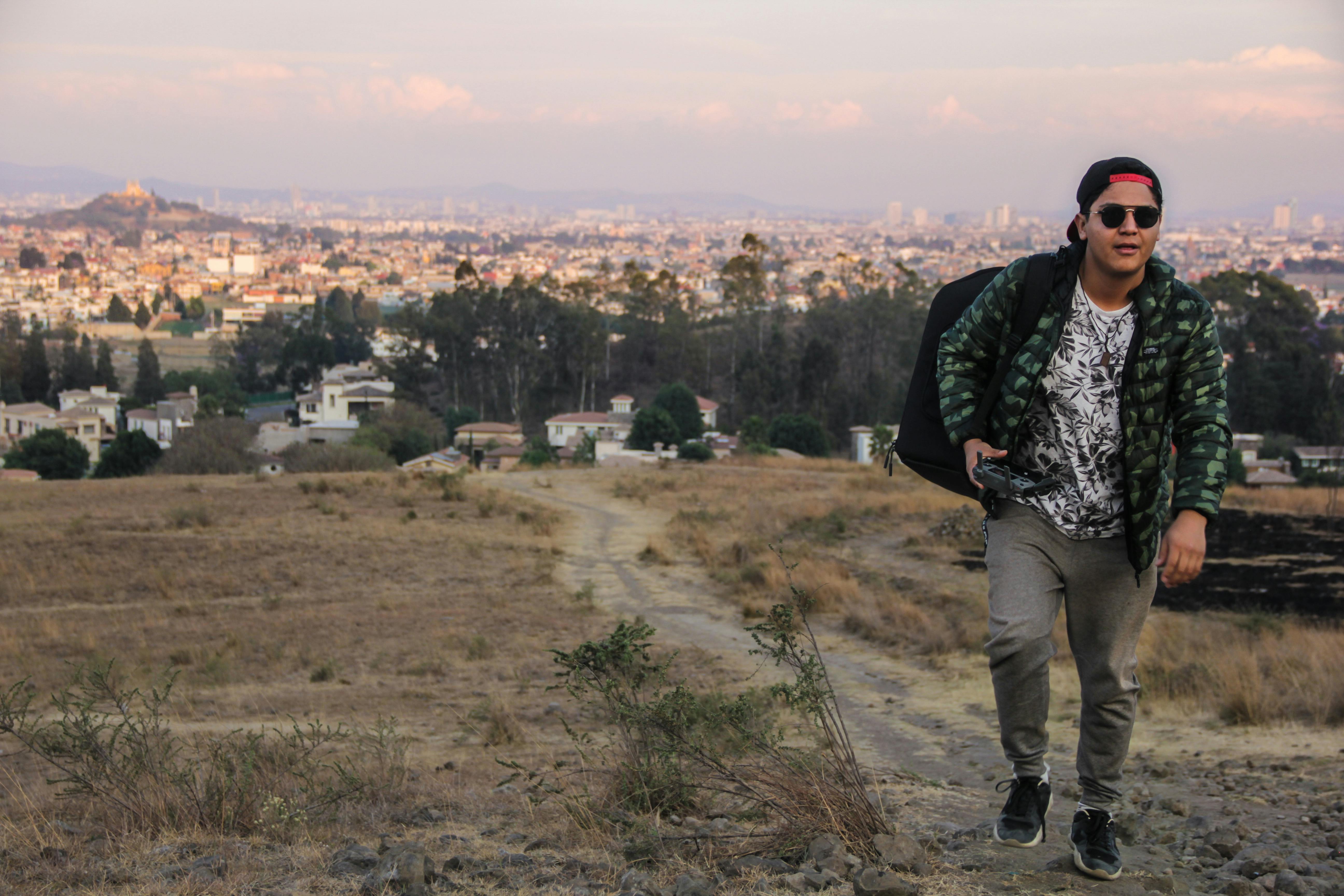 日落时分，在墨西哥乔卢拉，一名男子走过一片田野，田野上可见城市景观