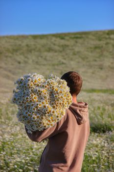 Young boy holding large daisy bouquet in rural sunny meadow.