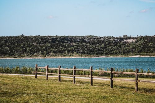 Free Serene view of a lake with a wooden fence and lush forest in the background. Stock Photo