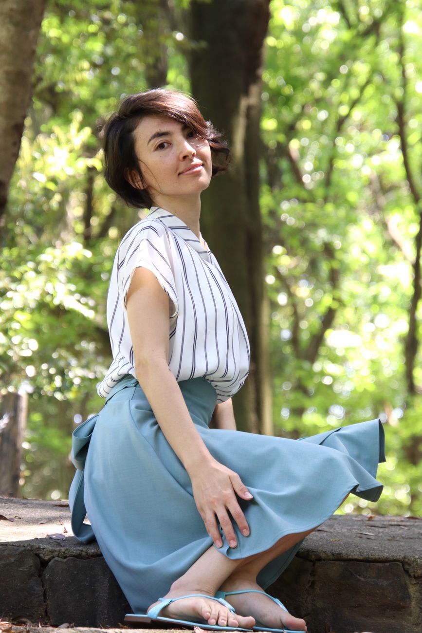 A young woman sitting outdoors in a sunlit forest, looking contemplative.