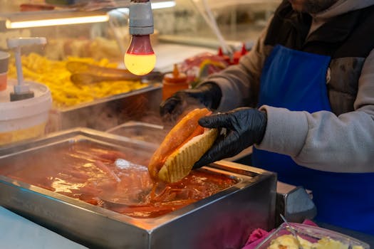 A street vendor prepares a hot dog with sauce at a bustling night market in Istanbul.