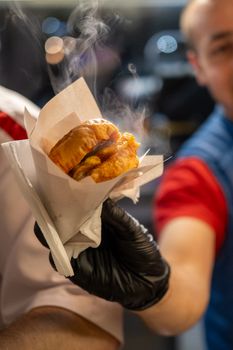 Close-up of a street vendor's hand offering a freshly made, steaming burger in Istanbul, Turkey.