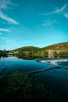 湖畔村庄绿树成荫，天空蔚蓝，景色宁静
