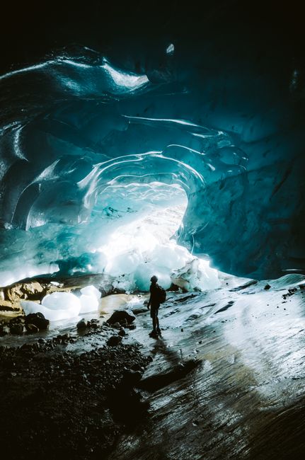 Silhouetted figure explores the stunning interior of a glacial ice cave.