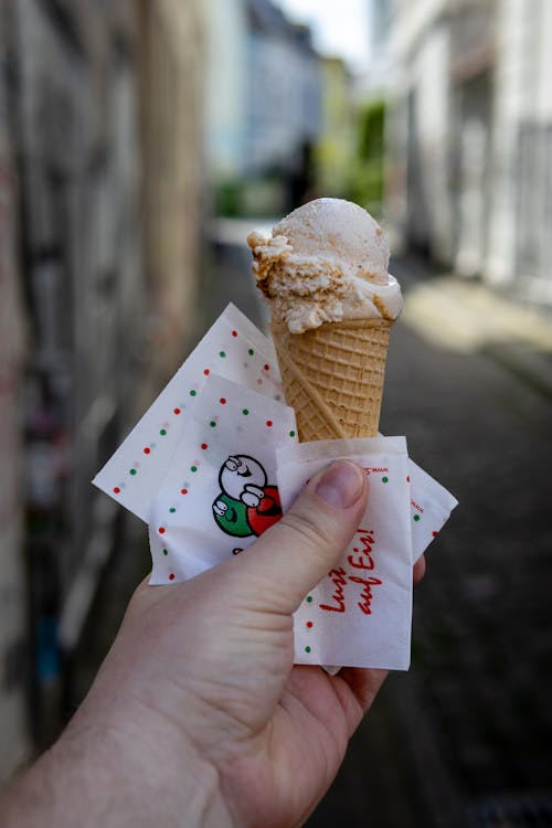 A hand holding an ice cream cone in a narrow alley