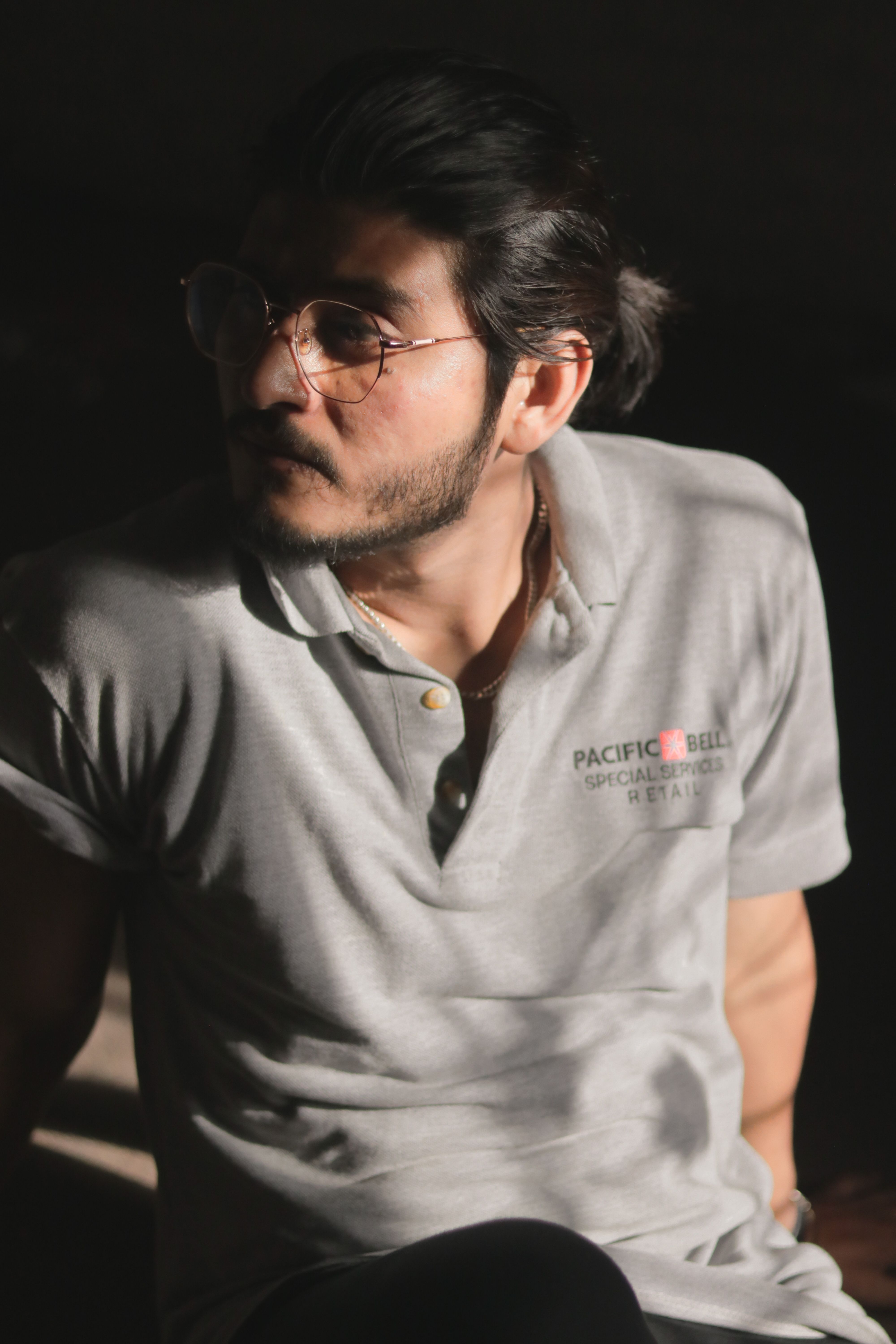 Fashionable man in glasses wearing a gray polo shirt in a studio setting.