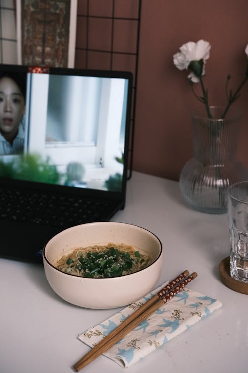 A bowl of ramen with chopsticks and a laptop