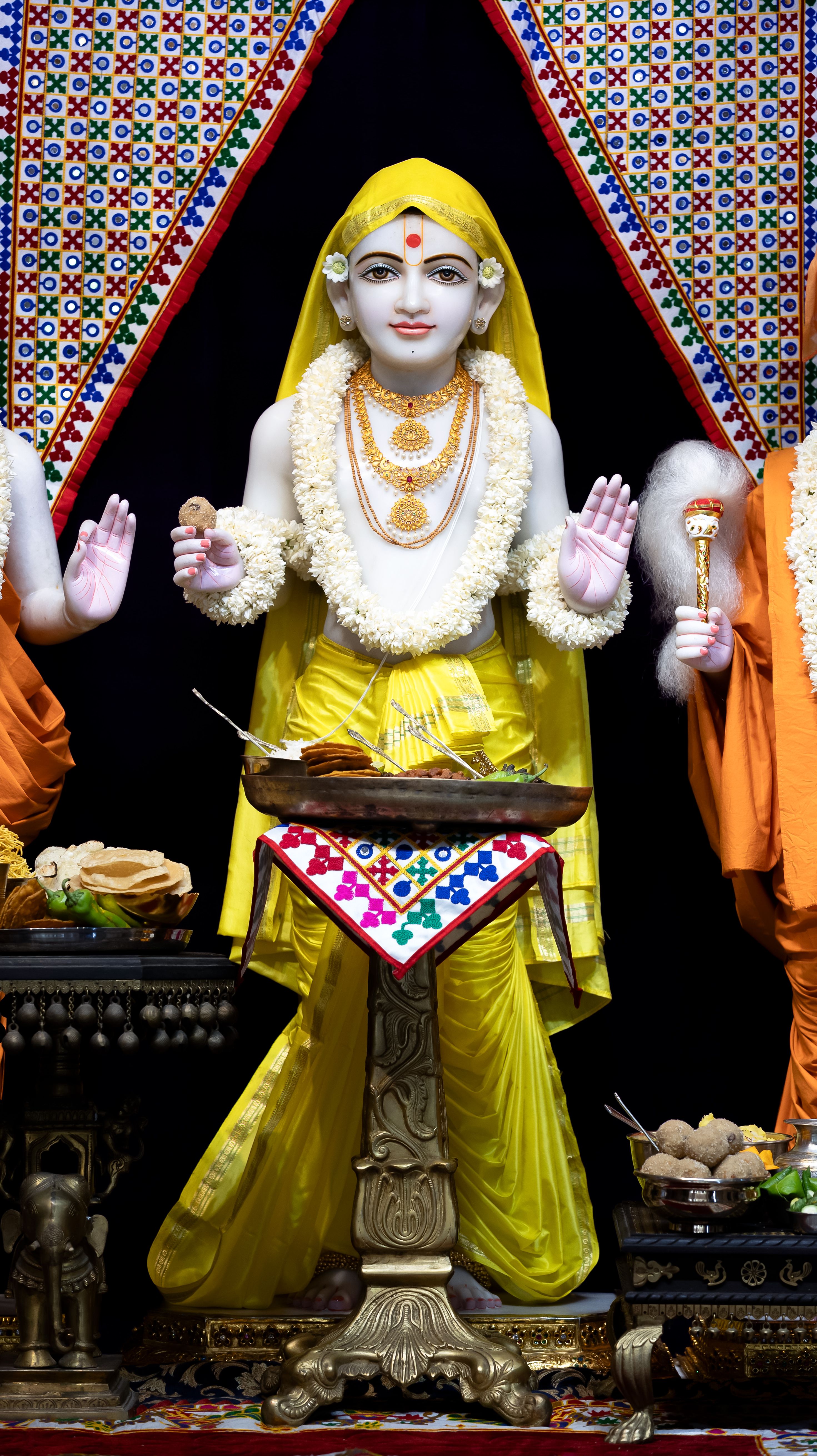 Intricately detailed statue of a Hindu deity in a Swaminarayan temple, adorned with yellow robes and garlands.