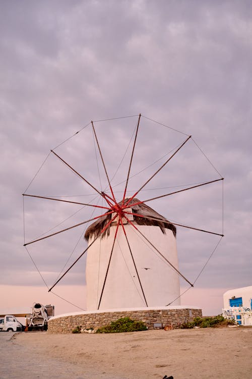 A windmill is on a beach with a cloudy sky