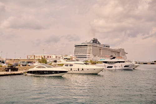 Several boats docked at a marina with a cruise ship in the background