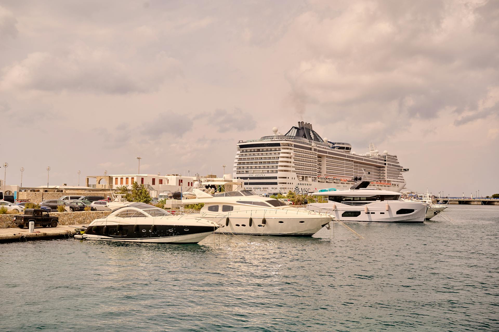 A scenic view of luxury yachts and a cruise ship moored at a bustling port under cloudy skies.