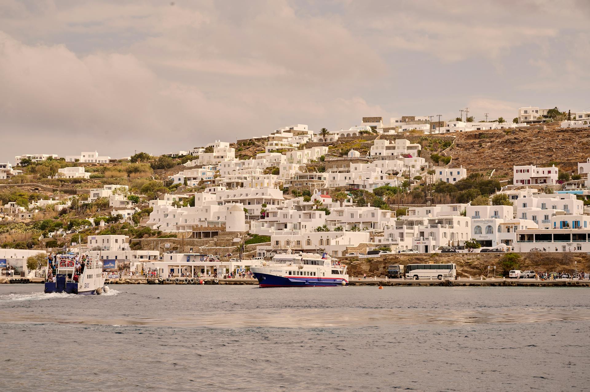 Charming coastal town with white buildings on a hill and ferries in the sea.
