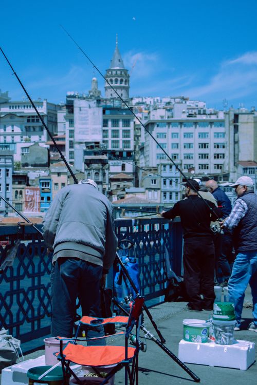 Free Men fishing on Istanbul's Galata Bridge with city skyline backdrop. Stock Photo