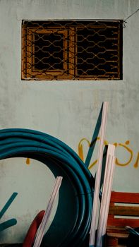 Industrial materials stacked against an old urban wall with a barred window, set in warm evening light.