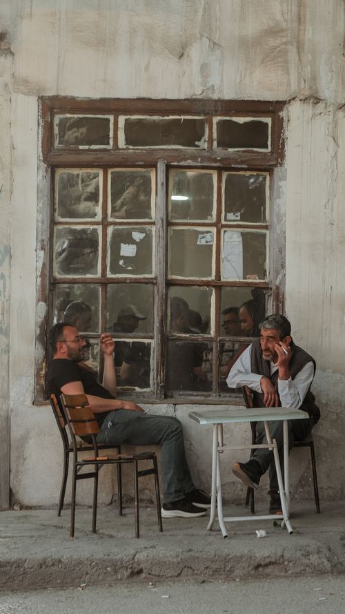 Free Two men smoking and talking outside a rustic cafe facade. Stock Photo