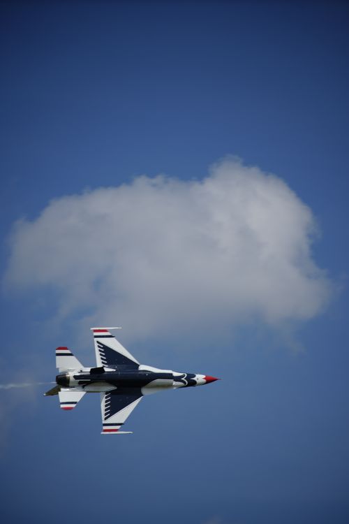 Free An F-16 fighter jet in flight against a vast blue sky with a single cloud. Stock Photo