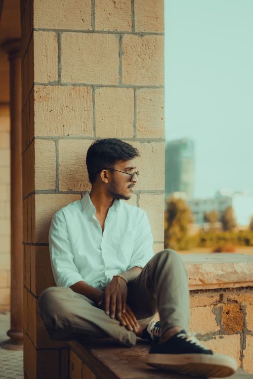Free A stylish man in casual attire sitting and gazing in a serene urban environment. Stock Photo
