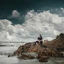 在孟买，一位沉思的女子坐在海边的岩石上，云层景观引人注目