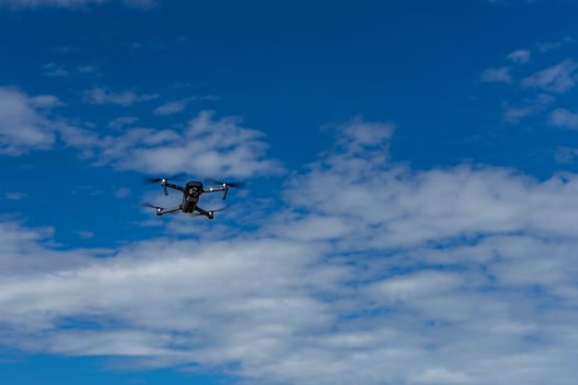 Aerial drone captured mid-flight against a vast blue sky with fluffy clouds.