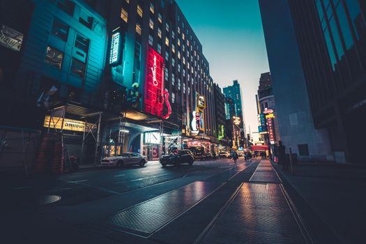 Dynamic urban scene in New York City captured at dusk, highlighting illuminated skyscrapers and lively streets.