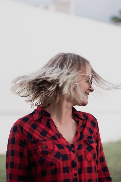 Photo of Smiling Woman in Red and Black Plaid Shirt Swinging Her Hair