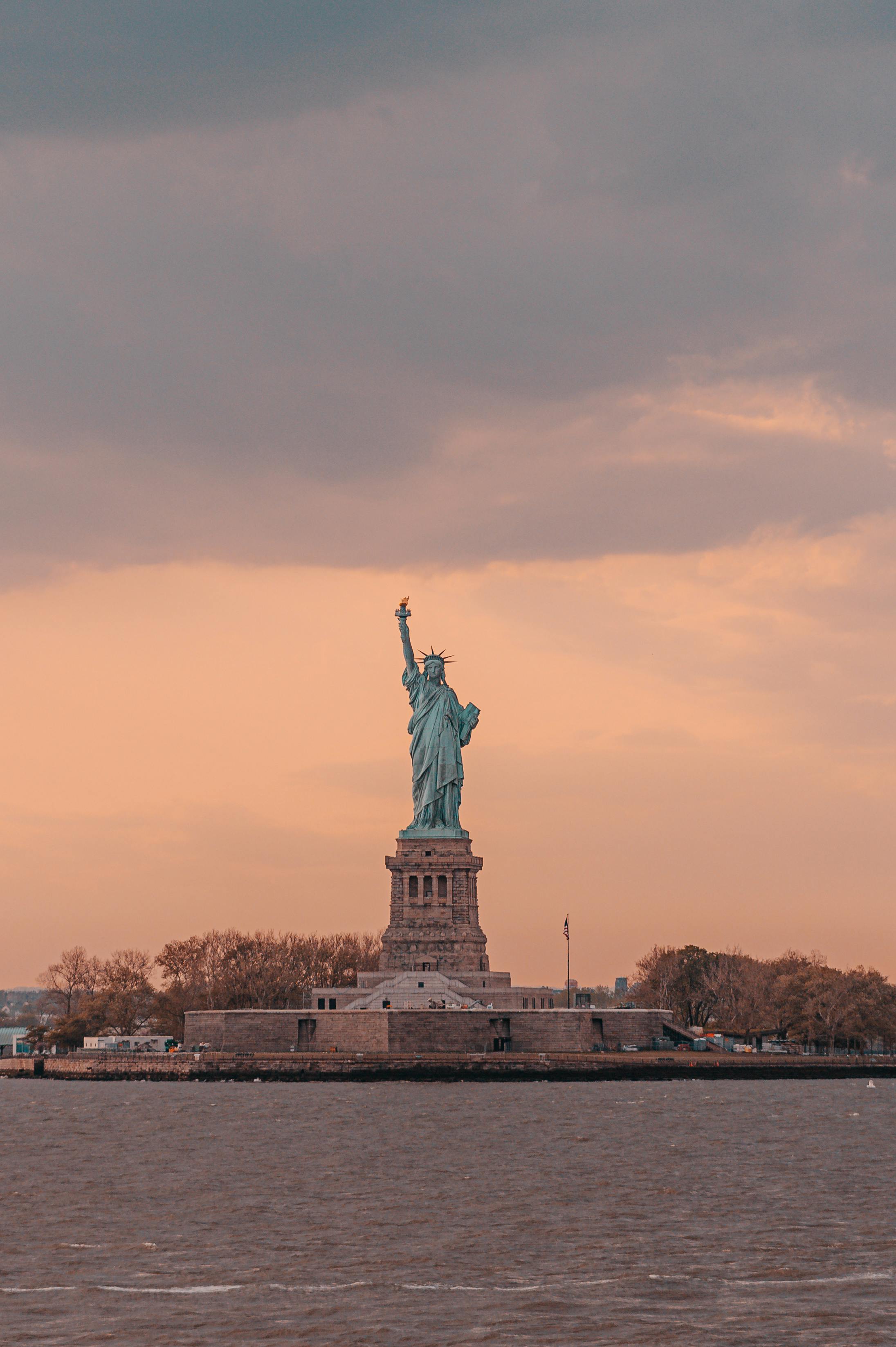 Beautiful view of the Statue of Liberty with a sunset backdrop, showcasing New York City's iconic landmark.