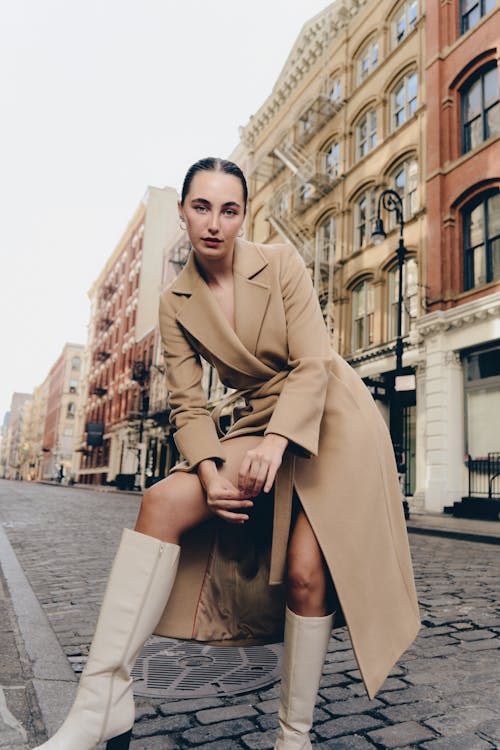 A woman in a trench coat and boots posing on a city street