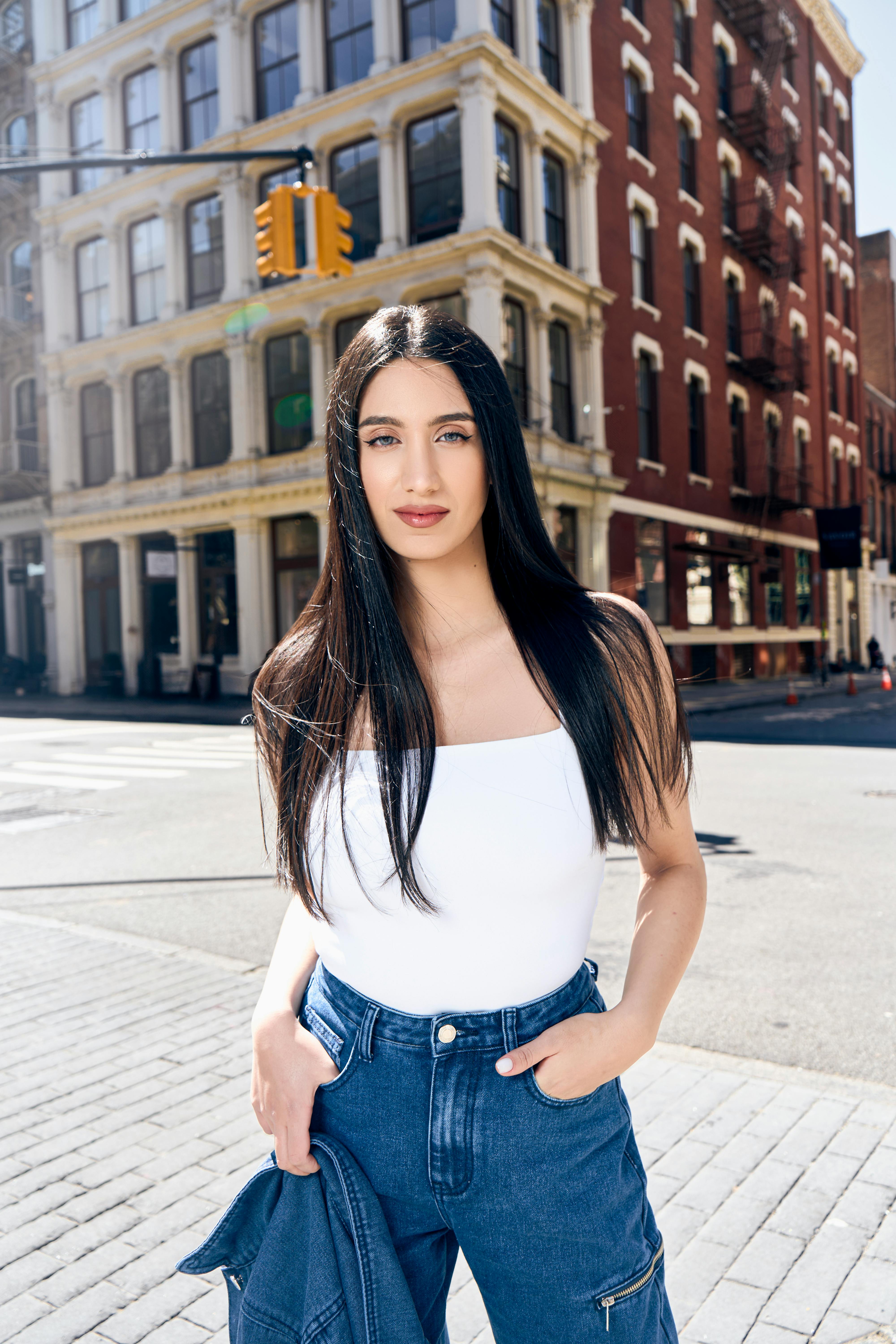 Free A woman in a white top and blue jeans standing on a street Stock Photo