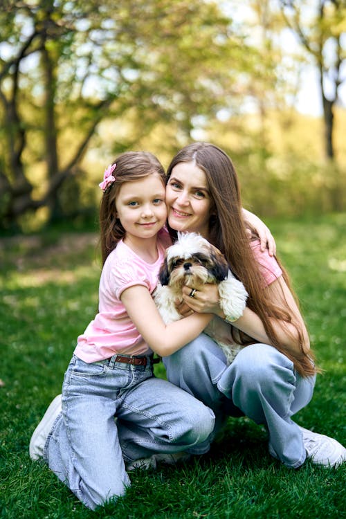 A woman and her daughter are hugging a dog