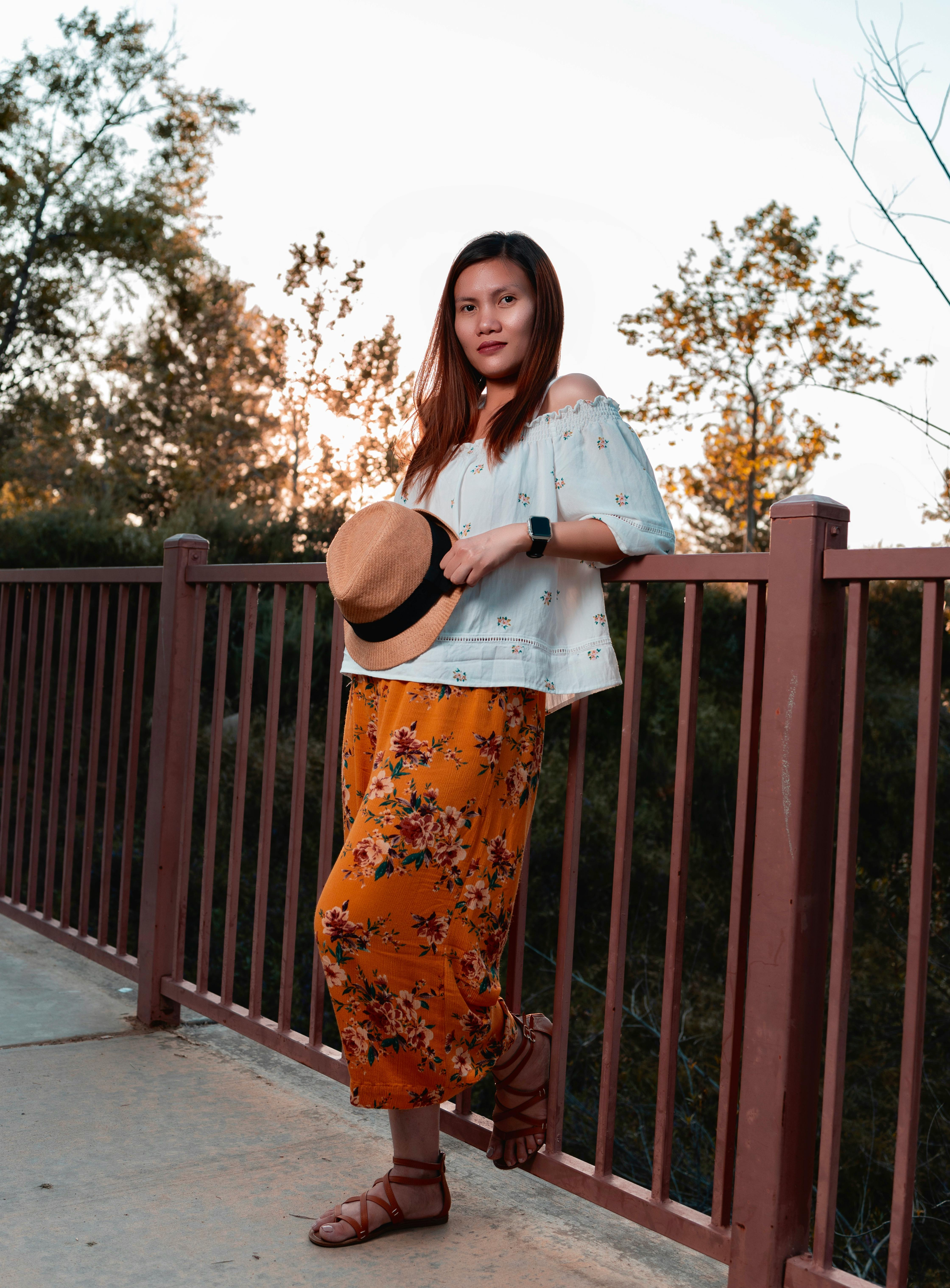 一位穿着花卉裙子、戴着帽子的时尚女子靠在栏杆上