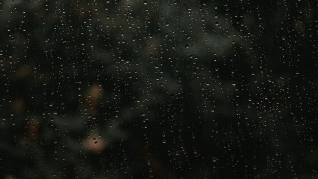 A close-up view of raindrops on a window with a blurred natural background, perfect for conveying a moody vibe.