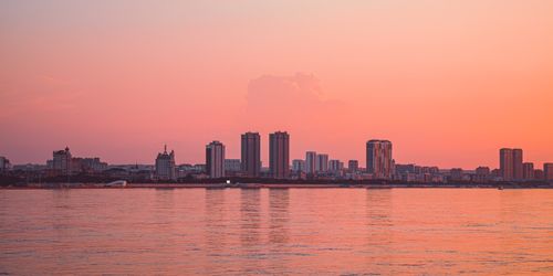 Free A tranquil city skyline reflecting in calm waters at sunset. Stock Photo