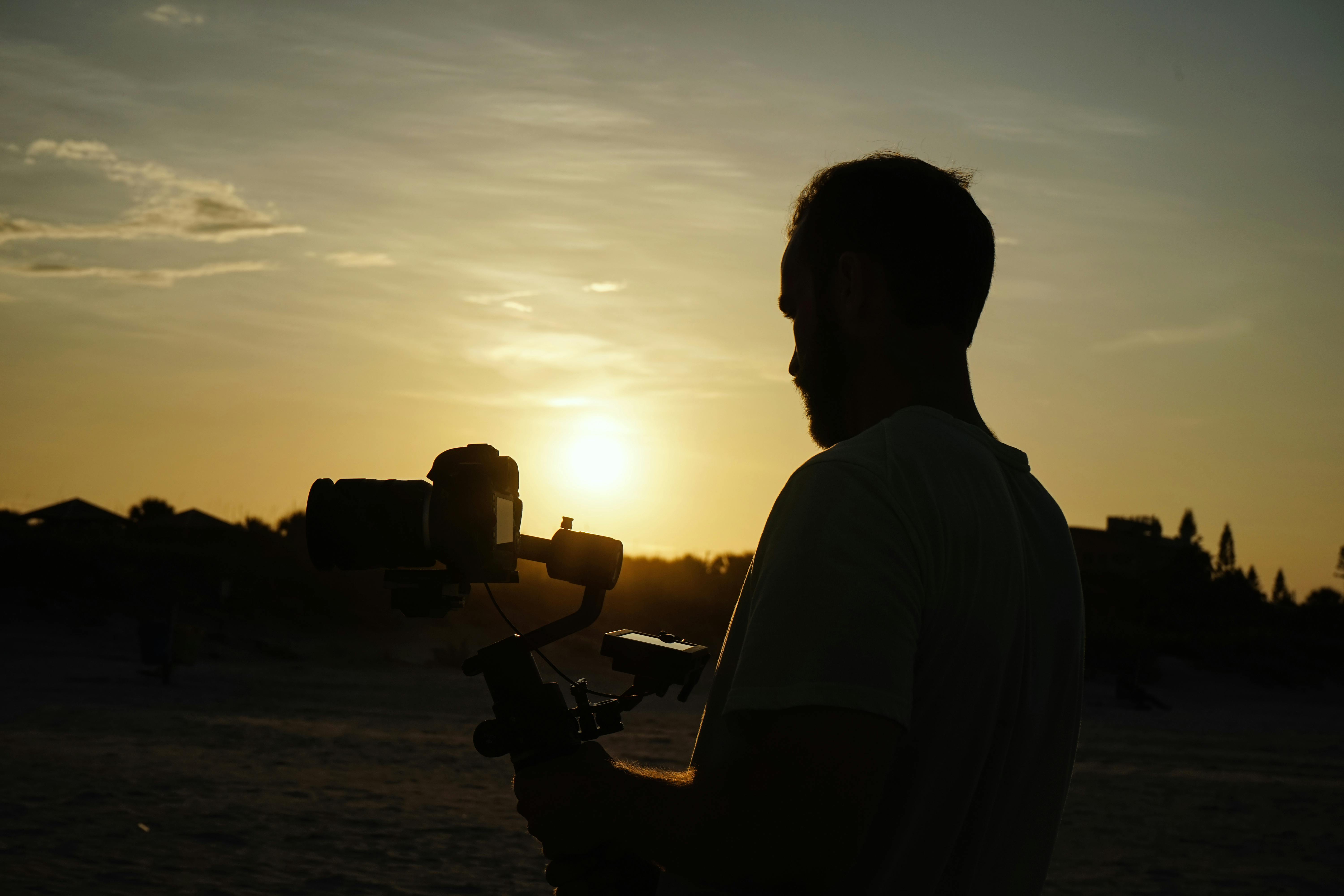 silhouette photo of man holding camera during golden hour