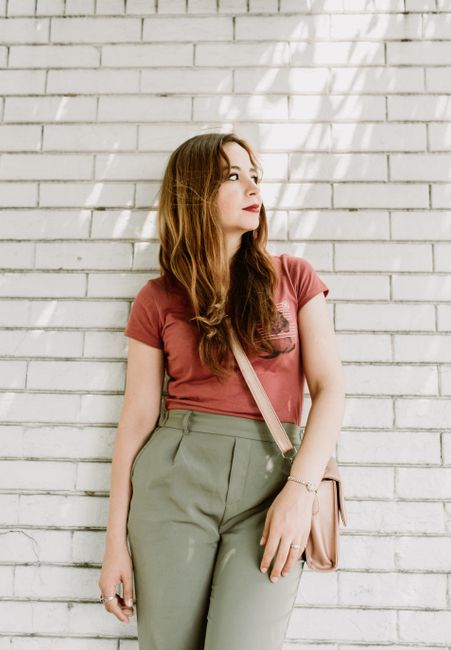 A stylish woman poses against a white brick wall under soft sunlight, showcasing casual fashion.