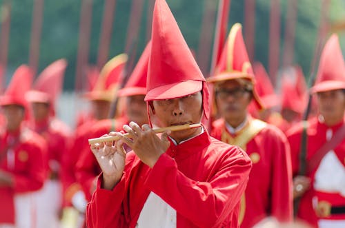 Man Wearing Red Hat and Uniform Playing Flute