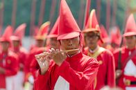 A colorful parade featuring musicians in traditional red costumes performing outdoors.