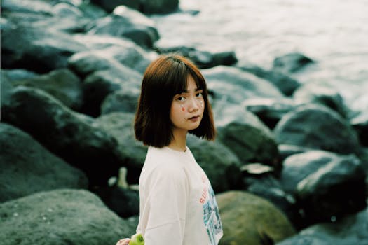 Portrait of a young woman with face paint standing on rocks by the sea. Captured in daylight.