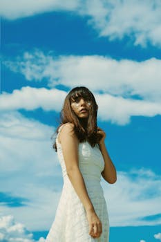 一位身着白色连衣裙的时尚女子在蓝天下摆姿，捕捉夏日气息