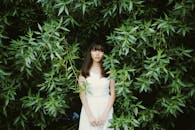 一位身穿白色连衣裙的年轻女子立于生机勃勃的绿叶间，自然与时尚之感油然而生
