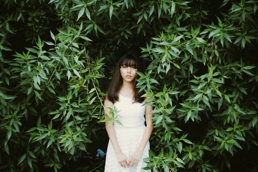 一位身穿白色连衣裙的年轻女子立于生机勃勃的绿叶间，自然与时尚之感油然而生