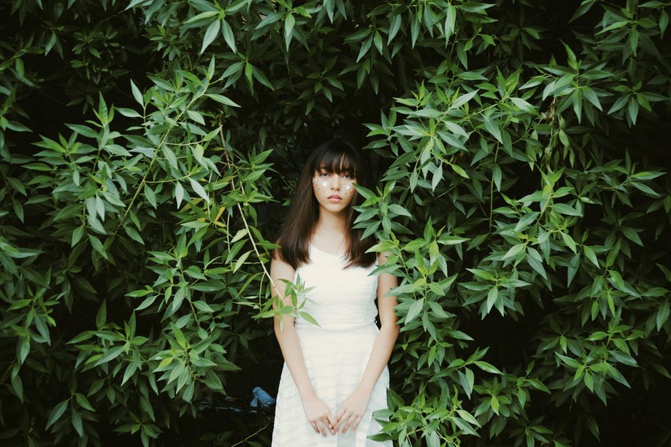 Young woman in white dress standing amidst vibrant green leaves, evoking a sense of nature and fashion.