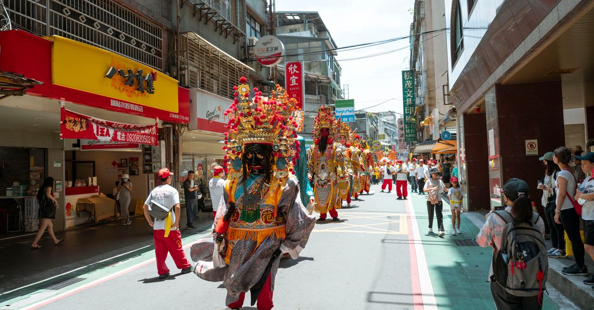 Colorful street festival parade with costumed performers in a bustling city street scene.