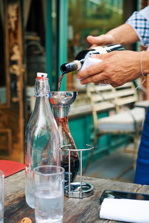Person Pouring Wine on a Clear Glass Bottle