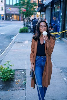 A woman enjoying an ice cream cone while strolling down an urban street in casual attire.