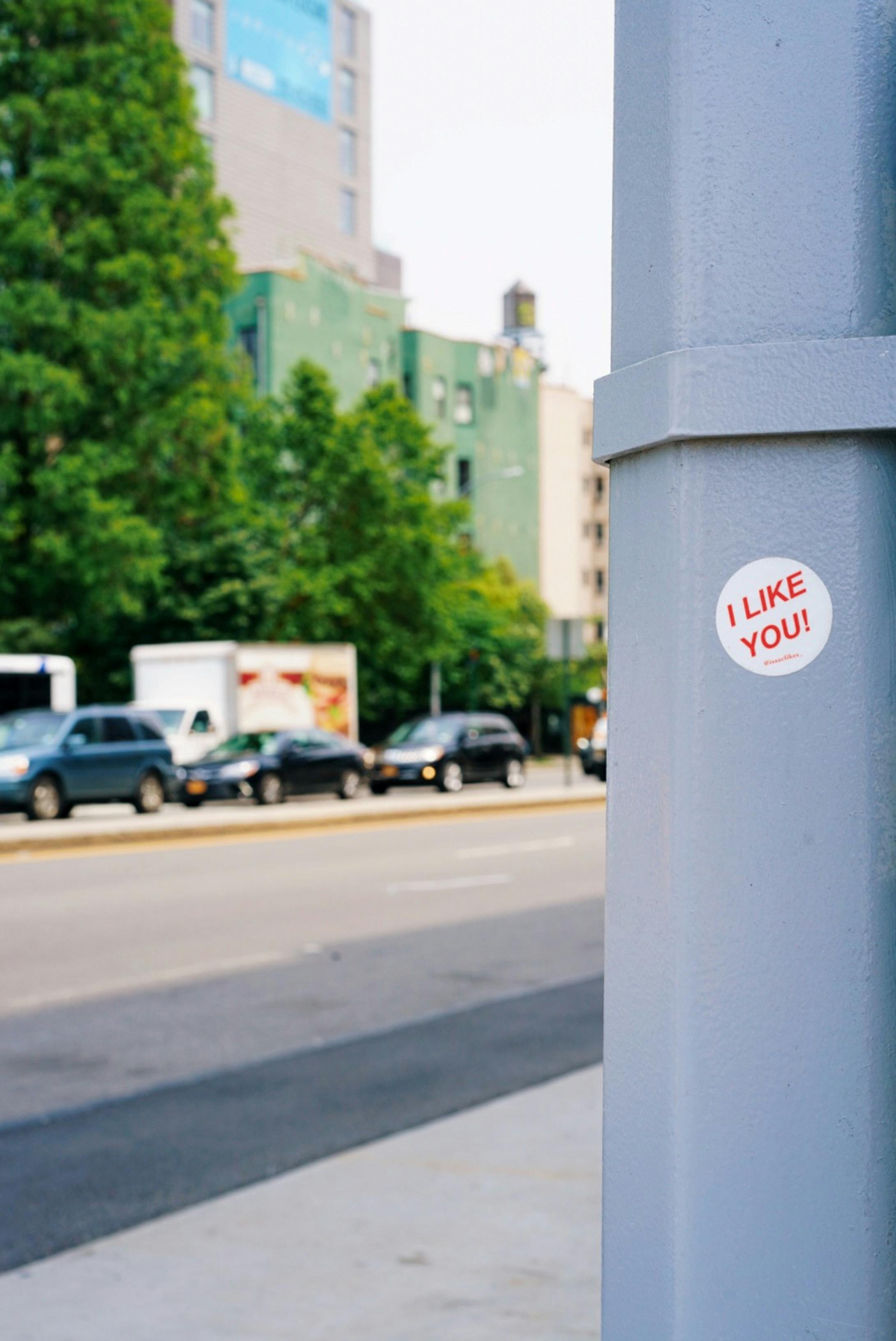 街景中，有汽车和杆子上贴着写有“我喜欢你！”的贴纸