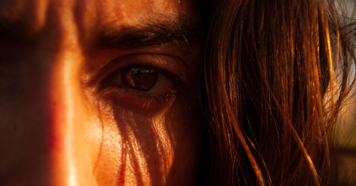 close-up of a person's face with morning sunlight hitting their eyes, soft focus on the sky in the background